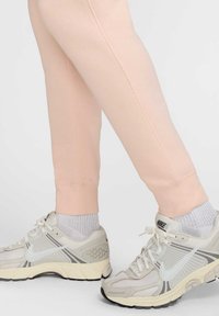 Pantalones de chándal rosa claro con dobladillos ajustados, combinados con zapatillas Nike beige y grises y calcetines blancos con canalé visibles en los tobillos.
