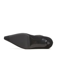 Black high-heeled shoe with a pointed toe, suede upper, textured rubber sole, and a subtle logo detail on the heel area.