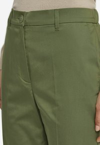 Olivgröna byxor med en slät textur, med knappstängning, bältesöglor och en sidoficka till vänster.