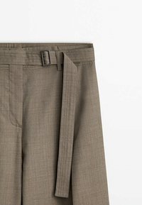 Gros plan sur un pantalon marron taille haute avec une ceinture en tissu passant à travers une boucle rectangulaire argentée.