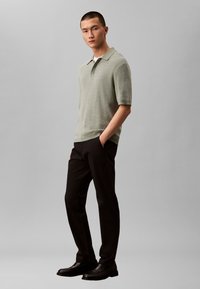 Tricou polo verde deschis, din tricot cu mâneci scurte și guler, asortat cu pantaloni negri slim-fit și pantofi negri. Design simplu, texturat.