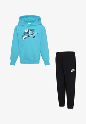 Sudadera Nike turquesa con un logotipo gráfico, combinada con pantalones de chándal negros que presentan un logotipo blanco. Ambos están hechos de un tejido suave y tienen puños acanalados.