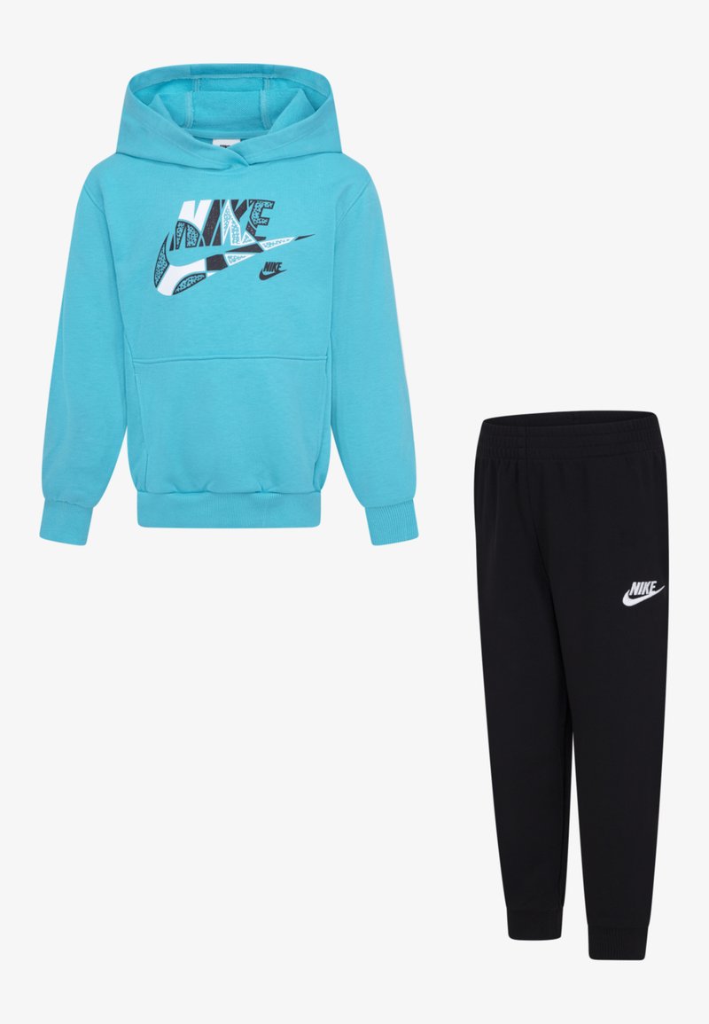 Tirkīza Nike kapuce ar grafisku logotipu, apvienota ar melniem sporta biksēm ar baltu logotipu. Abas ir izgatavotas no mīksta auduma un tām ir ribotas aproces.
