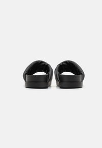 Des chaussures noires à enfiler avec un dessus rembourré, une semelle en caoutchouc plate et une forme arrondie, conçues pour le confort et la facilité d'enfilage.
