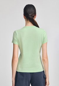 Camiseta de manga corta verde claro con cuello redondo. Textura suave y diseño ajustado, sin patrones visibles ni adornos.