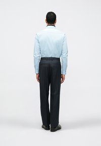 Camisa de manga longa azul-claro com gola escura, combinada com calças escuras riscas de giz. Os sapatos têm um design de sola robusta.