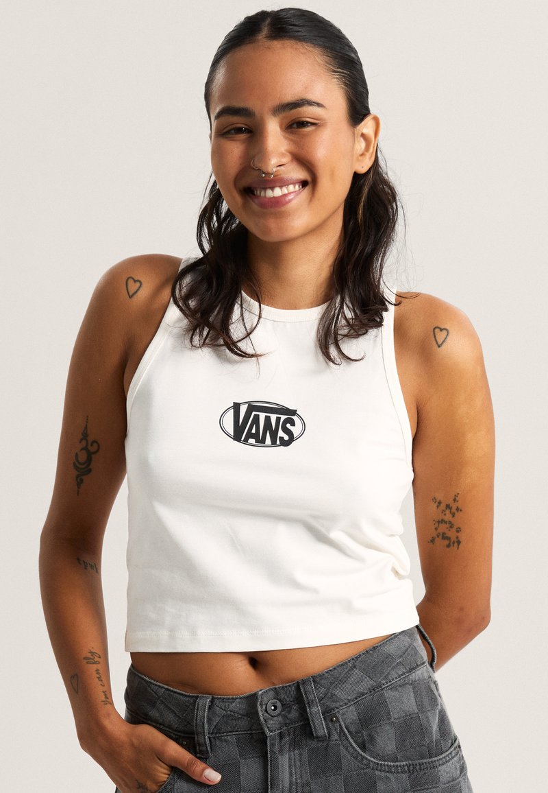 White cropped tank top with a black "VANS" logo at the center; paired with gray checkered high-waisted pants. Patterns on arms are visible.