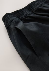 Crne hlače od tkanine s elastičnim pojasom, glatke teksture i jednostavnog dizajna. Nema istaknutih uzoraka ili ukrasa.