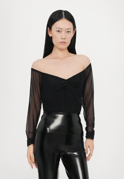 Sort off-shoulder top med gennemsigtige lange ærmer og en snoet frontdetalje, parret med høj talje glinsende sorte leggings.