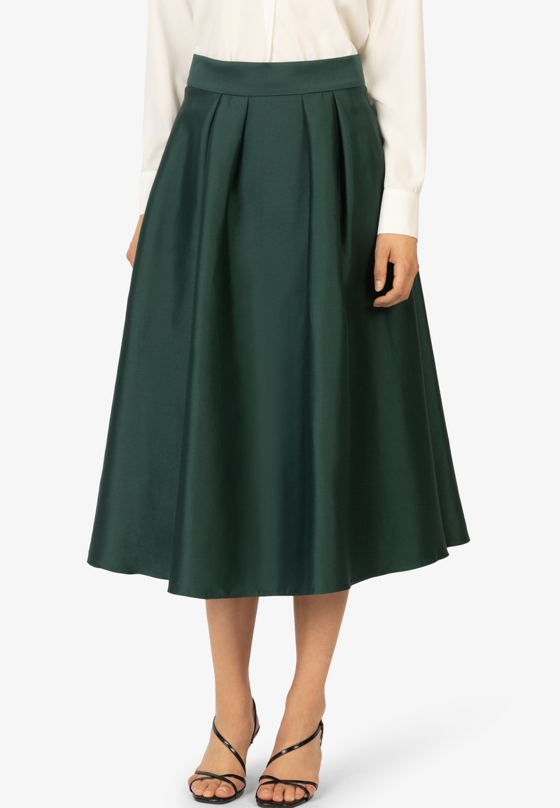 Donkergroene midi-rok met plooien, een aansluitende tailleband en een zachte satinstructuur. Gepaard met zwarte sandalen met bandjes.