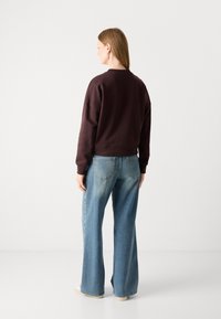 Sudadera marrón corta con un cuello redondo, combinada con unos vaqueros de pierna ancha de color azul claro, que presentan una textura desvanecida y bolsillos traseros.
