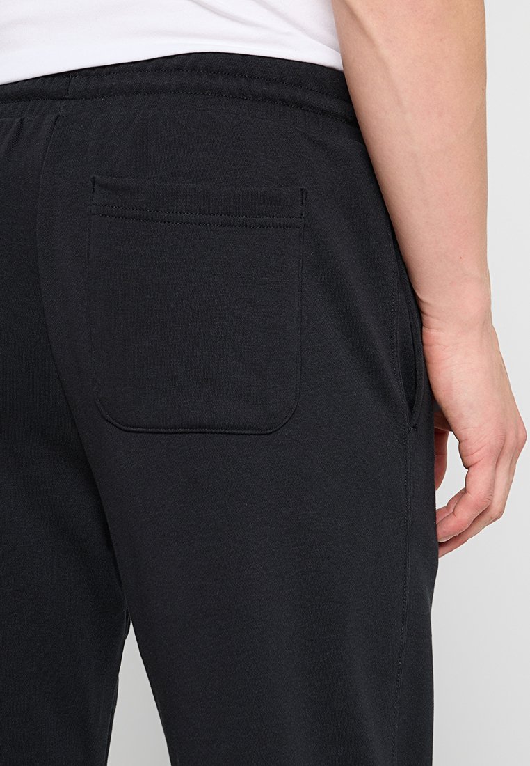 Pantaloni sportivi neri realizzati in tessuto morbido, con una tasca posteriore e un cinturino elastico. Texture liscia con dettagli di cuciture minime.