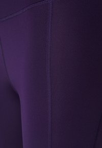 Purple leggings made of smooth, stretchy fabric, featuring flat seams along the sides without pockets or additional embellishments.