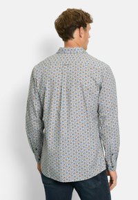 Mann, der von hinten schaut, trägt ein langärmliges Hemd mit einem mehrfarbigen abstrakten Wirbelmuster und dunkelblaue Jeans.