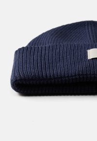 Gorro de malha azul-marinho com textura canelada e dobra na bainha. Apresenta uma pequena etiqueta de tecido retangular de lado.