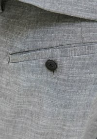 Grå linnbyxor med en texturerad finish, försedd med en sidficka och en svart knapppunkt.