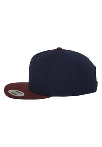 Marineblaue Kappe mit einem kastanienbraunen Schirm, strukturiertem Design und texturiertem Stoff. Verfügt über Belüftungslöcher und einen verstellbaren Riemen auf der Rückseite.
