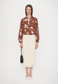 Bruine bloemenblouse met een knoop-nek, gecombineerd met een witte kanten rok met een geschulpte onderrand en een zwarte handtas. Wit puntige schoenen.