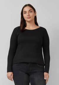 Schwarzes Langarmoberteil mit rundem Halsausschnitt, hergestellt aus weichem Stoff. Glatte Textur, figurbetonte Silhouette und minimalistische Nähte entlang der Schultern.