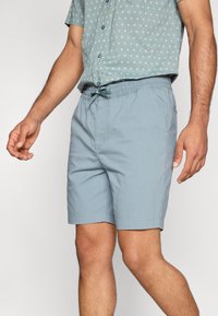 Ανοιχτό μπλε σορτς από απαλό ύφασμα, με ελαστική μέση και κορδόνι. Δύο πλαϊνές τσέπες και ίσια κοπή.