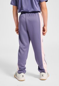 Lilla sportbukser med en lyserød sideliste, elastisk talje og glat tekstur. Kombineret med lysefarvede sneakers med synligt mærke.