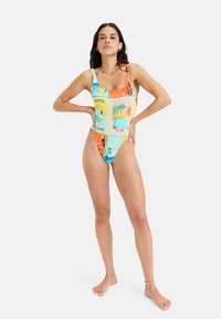 Maillot de bain une pièce multicolore avec un motif graphique vibrant. Il présente un décolleté carré, des jambes échancrées et une texture de tissu lisse et élégante.