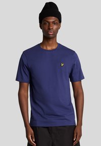 T-shirt di cotone blu navy con scollatura a girocollo e maniche corte. Presenta un piccolo logo giallo sul lato sinistro del petto. Texture liscia.