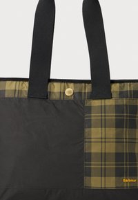 Bolsa tote preta com um painel xadrez caqui, alças de nylon preto resistentes e um botão de pressão dourado. Logótipo da marca em laranja de um lado.