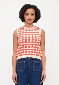 Débardeur en tricot sans manches avec un motif géométrique en corail et crème, avec un col et un ourlet côtelés. Assorti à un jean en denim taille haute.