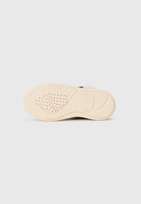 Sól sneakeru s textúrovaným krémovým gumovým dnom s vlnitým vzorom a ventilačnými otvormi, navrhnutá pre priľnavosť a flexibilitu.
