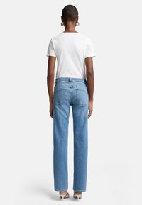Jeans blue a vita alta con un design a gamba dritta, realizzati in denim, dotati di tasche posteriori e un lavaggio chiaro. Abbinati a una maglietta bianca.