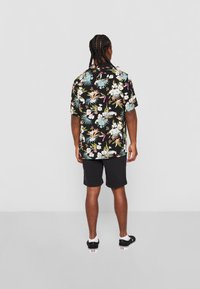 Camisetta nera a maniche corte con un vivace motivo floreale in rosa, blu e verde, abbinata a pantaloni corti neri e scarpe slip-on nere.