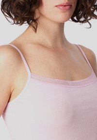 Light pink camisole featuring thin straps, a square neckline, and delicate lace trim along the top edge. Soft, stretchy fabric.
