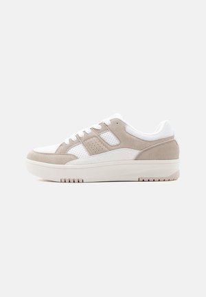 Lage sneaker met beige suède en witte mesh panelen, witte veters en een dikke witte zool, vanaf de zijkant getoond op een witte achtergrond.