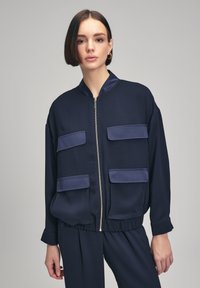 Giubbotto bomber blu navy realizzato in tessuto liscio, con zip frontale, due grandi patte per le tasche e polsini a coste, dal taglio morbido.