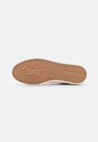 Rubber outsole with a patterned texture in light brown, featuring a horse graphic and "MUSTANG" logo; white midsole and gray top.