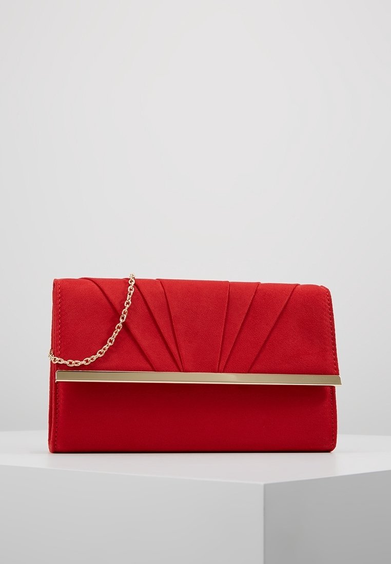 Pochette rouge avec design plissé, bandoulière chaîne dorée et détail barre dorée horizontale, posée sur une surface blanche sur fond neutre.