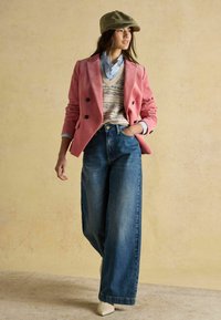 Ružový manšestrový dvojradový blejzer, vzorovaný pletený sveter, svetlomodrá košeľa, široké modré džínsy a biele lodičky so špicatou špičkou.