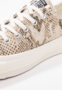 Sneaker low-top con tessuto a stampa serpente beige e marrone, lacci bianchi, occhielli in metallo e suola in gomma spessa avorio.
