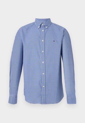 Sinine-valge ruuduline pikkade varrukatega särk nööpidega, nööpidega kaeluse ja väikese logoga vasakul rinnal.