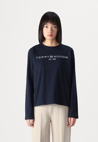 Sötétkék, hosszú ujjú pamut póló, melyen a mellrészen fehér színű "TOMMY HILFIGER EST. 1985" felirat található. Egyenes szabású dizájn.