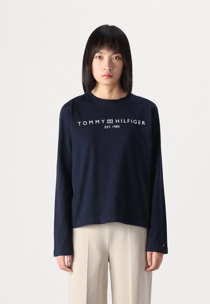 Sötétkék, hosszú ujjú pamut póló, melyen a mellrészen fehér színű "TOMMY HILFIGER EST. 1985" felirat található. Egyenes szabású dizájn.
