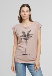 T-shirt en coton rose clair avec des manches retroussées, présentant un graphique de palmier noir et le mot "forêt" dans une police décontractée en bas.