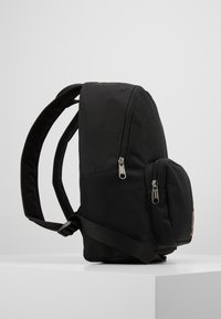Czarny plecak z tkaniny w zaokrąglonym kształcie, z dwiema zasuwanymi kieszeniami, wyściełanymi ramiączkami oraz detalem logo z przodu.