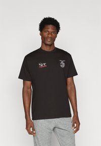 T-shirt preta de algodão com mangas curtas, apresentando texto branco e vermelho "Ser" e "Bourgeoisie" e um gráfico no peito.