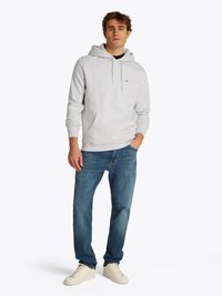 Lichtgrijze hoodie met trekkoord, gemaakt van een katoenmix, met een voorzak. Gecombineerd met blauwe jeans en witte sneakers.