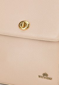Borsa in pelle testurizzata rosa chiaro con un bottone circolare dorato. Presenta un bordo cucito e un logo impresso nella parte inferiore.