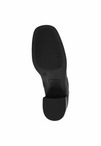 Črna guma podplat čevlja z teksturirano površino in rahlim peto, vsebuje odtis logotipa in zaobljene robove za stabilnost.