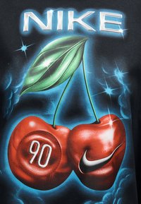 Δύο κόκκινα κεράσια με πράσινους μίσχους και φύλλο, το ένα κεράσι σημαδεμένο με "90" και το άλλο με ένα ασημί λογότυπο της Nike, πάνω σε μπλε καπνιστό φόντο.