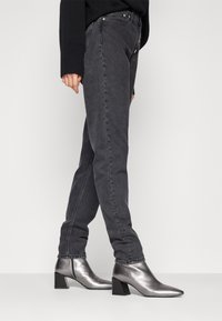 Šedé džíny s rovnými nohavicemi, kombinované s metalickými stříbrnými kotníkovými botami na blokovém podpatku a špičatou špičkou.